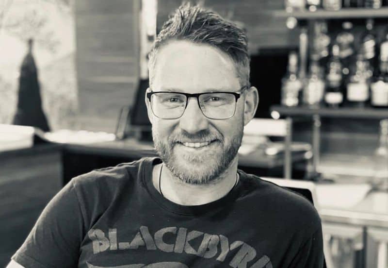 Aindriú Burgess ag caitheamh spéaclaí ag miongháire