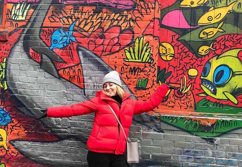 Cerise Thoor 0005 Img 0864 Cerise Thoor en manteau rouge, les bras tendus devant un mur avec des graffitis