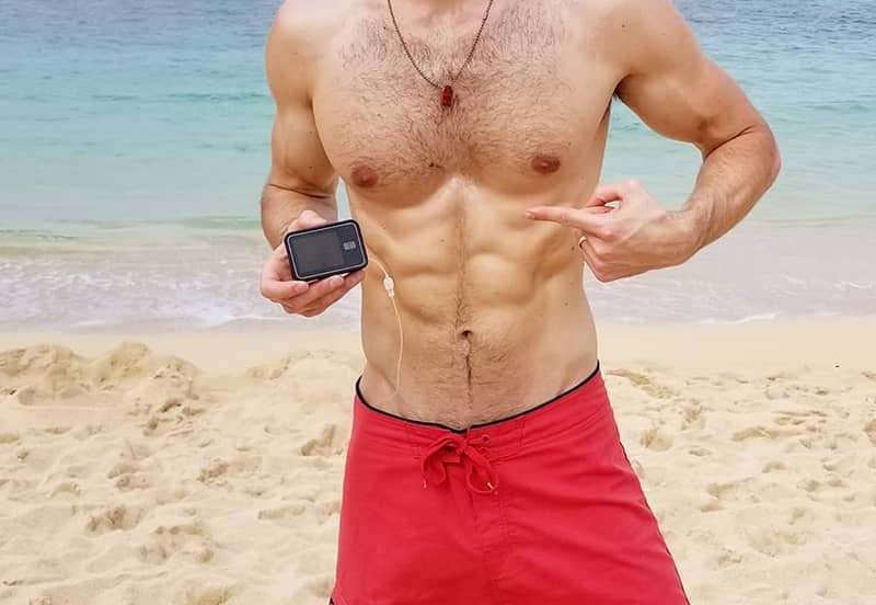 Matt Vande Vegte Pointing At His Insulin Pump On A Beach