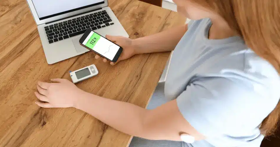 Woman With Glucose Sensor Using Mobile Phone For Measuring Of Blood Sugar Level At Home Woman With Glucose Sensor Using Mobile Phone For Measuring Of Blood Sugar Level At Home